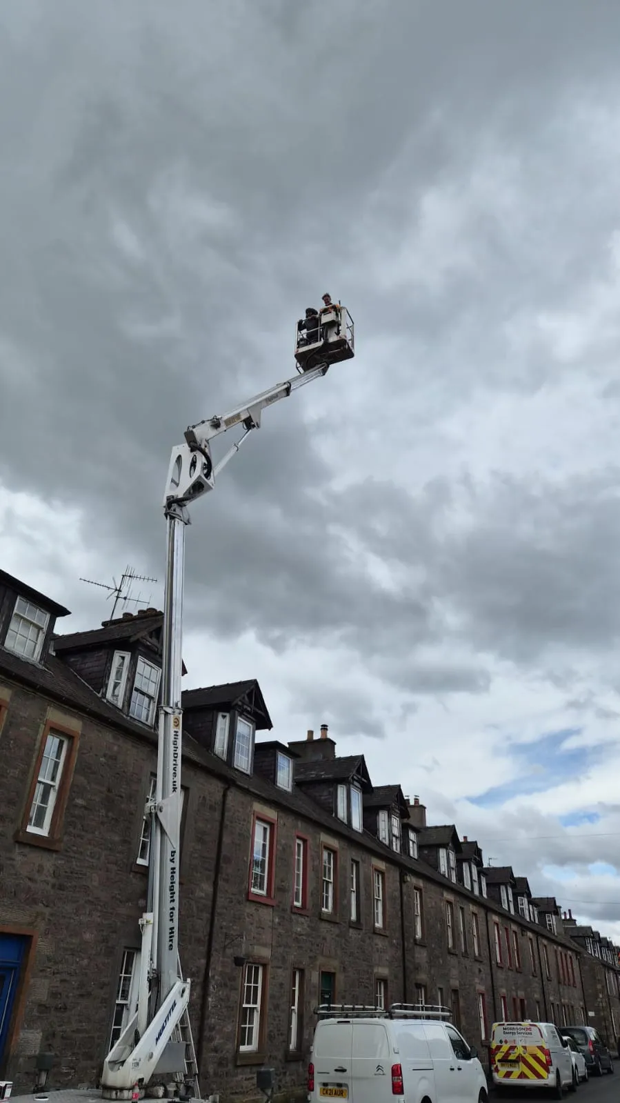 Cherry picker fully extended to reach the upper dormers of a stone tenement in Alloa