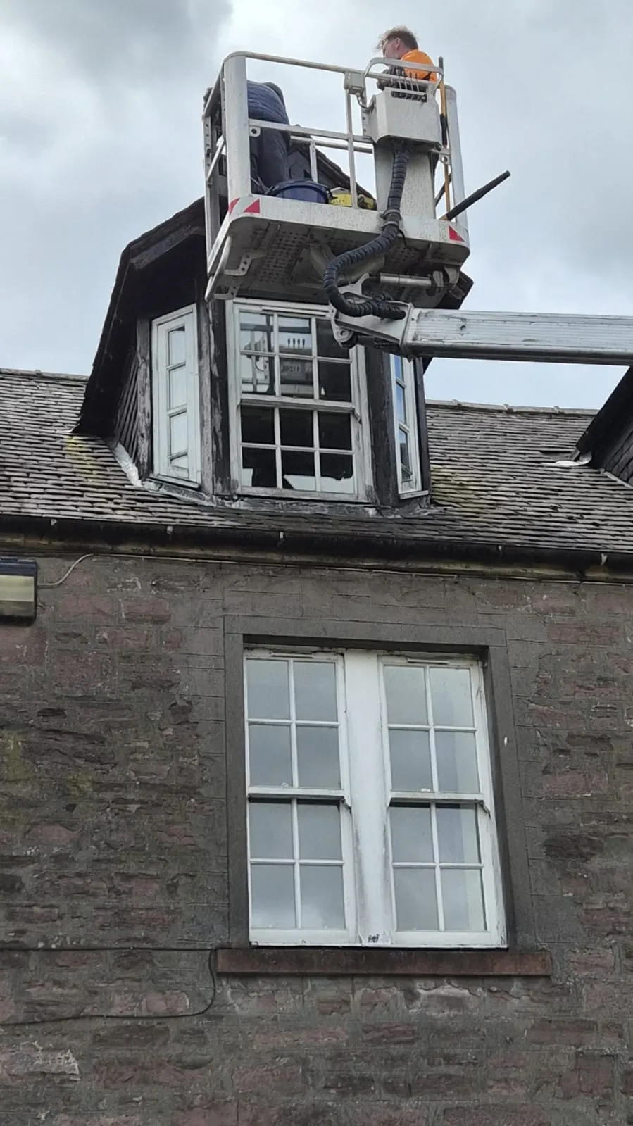 Cherry picker basket positioned over a dormer window during repair work in Alloa