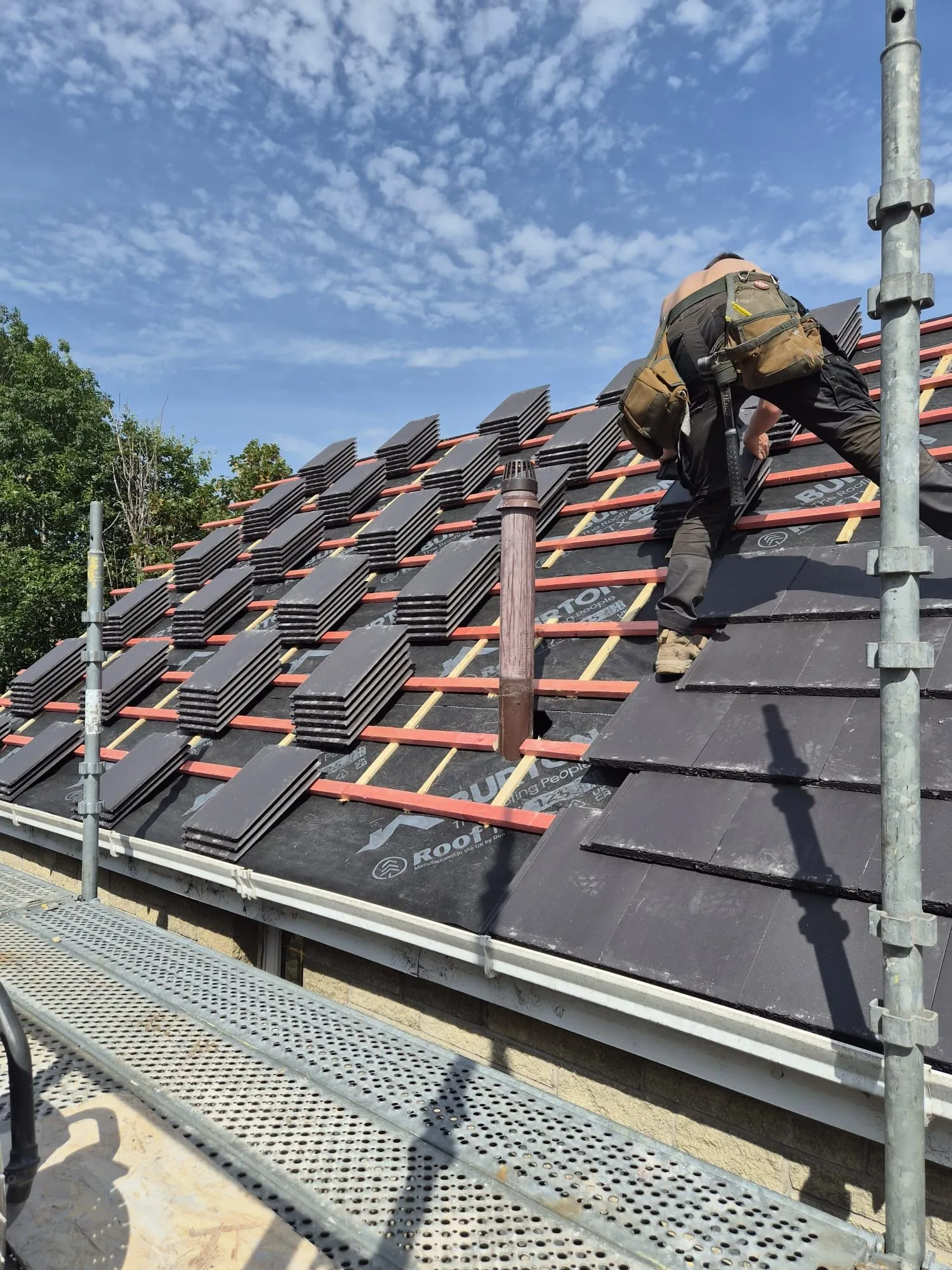 Roofer laying new tiles around a roof vent pipe on a house re-roof in Dalgety Bay, Fife