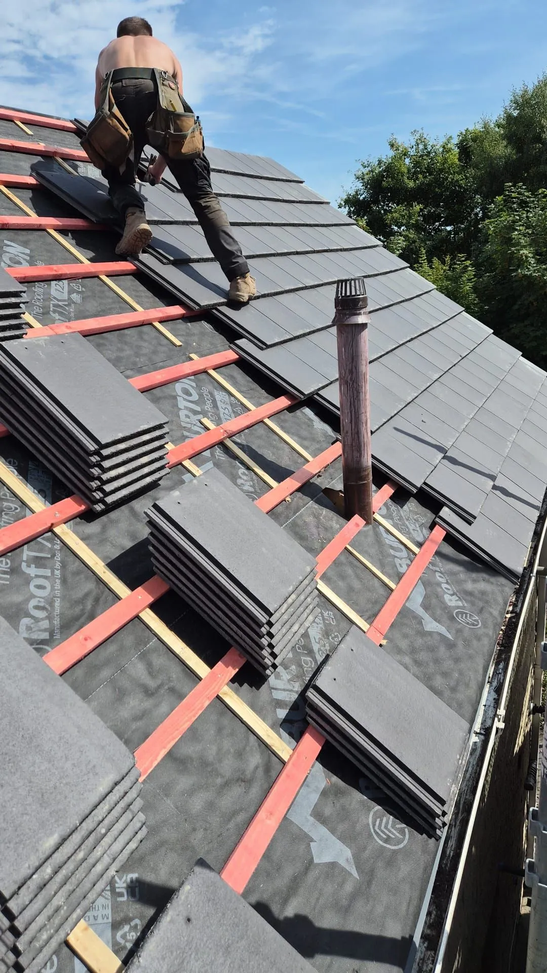 Roofer laying new slate grey tiles across the slope of a re-roof in Dalgety Bay