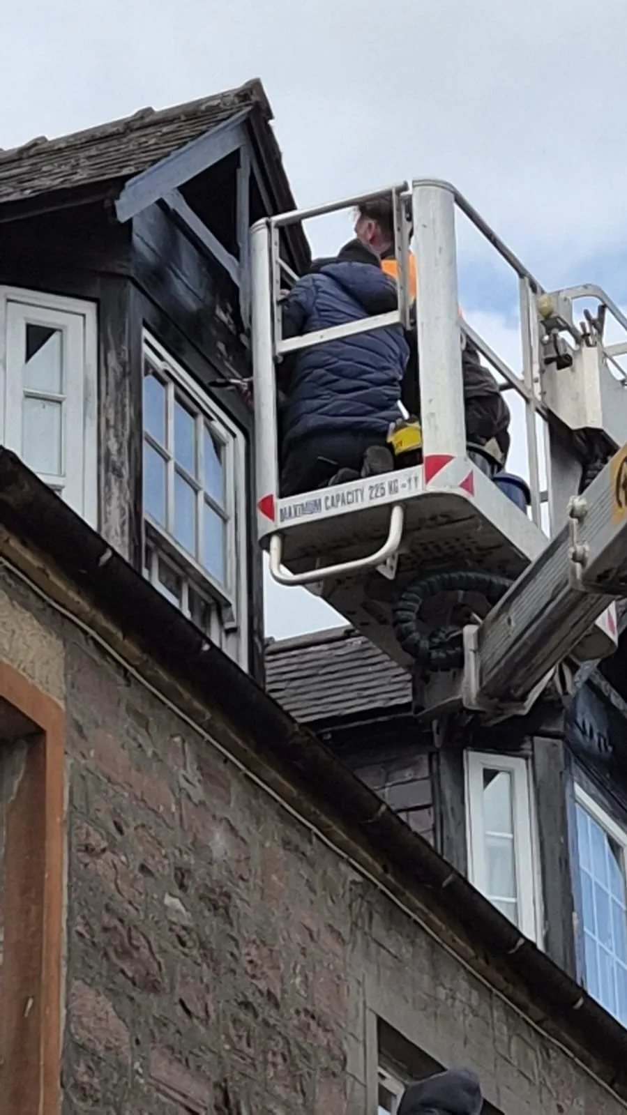 Two roofers working from a cherry picker basket to repair a dormer on a stone tenement in Clackmannanshire